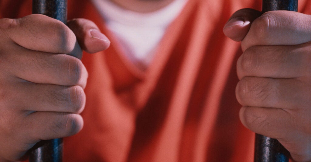 A man in an orange jumpsuit holds bars