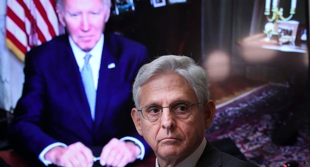 Merrick Garland in a suit with President Joe Biden towering over him