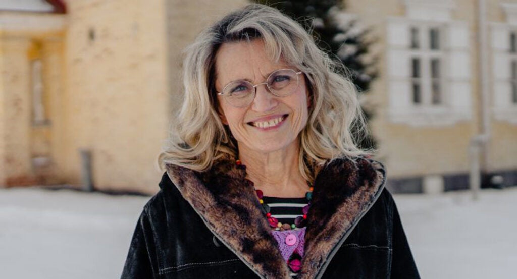 Päivi Räsänen in a black coat stands in front of a church building wearing glasses