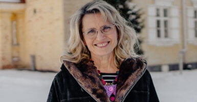 Päivi Räsänen in a black coat stands in front of a church building wearing glasses