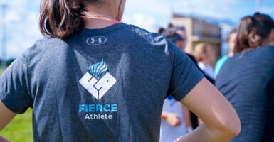 A woman stands on the edge of a sports field in a FIERCE Athlete t-shirt.