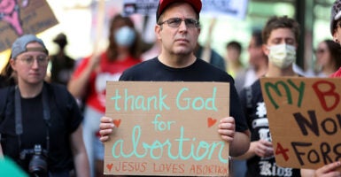 A man in a black shirt holds a sign reading "Thank God for abortion"