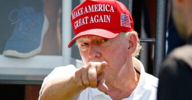 Donald Trump, wearing a "Make America Great Again" hat, points at the camera.