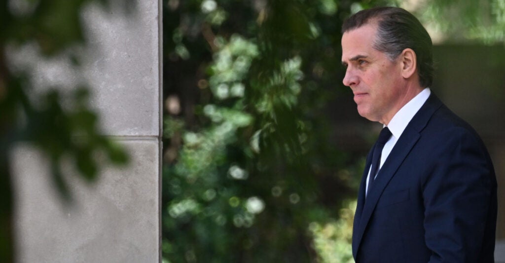 Hunter Biden in a suit walks in front of foliage