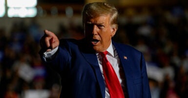 Former President Donald Trump points to the crowd in a dark blue suit and red tie during a political rally.