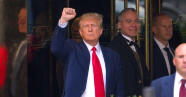 Donald Trump wears a blue suit jacket and a red tie. He holds up his fist.