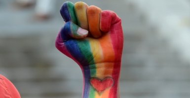 A fist painted in rainbow flag colors with a heart on the wrist