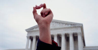 A hand raised in the air in front of the Supreme Court building holds a small plastic baby representing a child in the womb