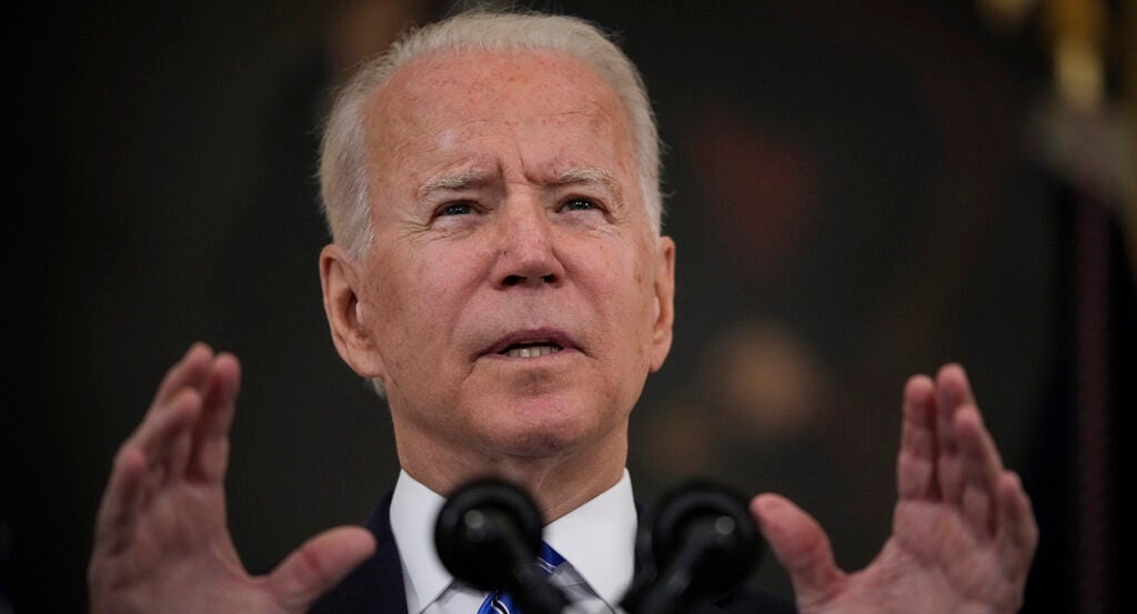 President Joe Biden gestures in front of a microphone while wearing a suit and a blue striped tie