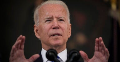 President Joe Biden gestures in front of a microphone while wearing a suit and a blue striped tie