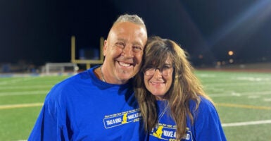 Coach Joe Kennedy and his wide Denise stand on the football field and smile.