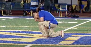 Coach Joe Kennedy kneels in prayer in the middle of the Bremerton High School football field.