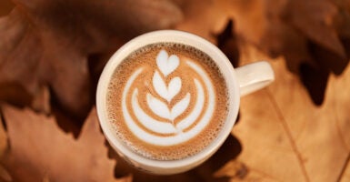 Fall leaves are seen on a table beneath a pumpkin spice latte.