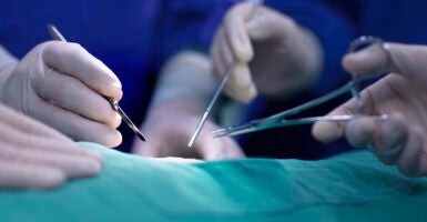 Doctors' hands hold surgical implements above skin