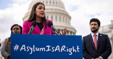 Rep. Alexandria Ocasio-Cortez speaks at a podium with a sign saying “Asylum is a right.”