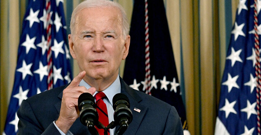 President Joe Biden speaks at a podium with US flags in background