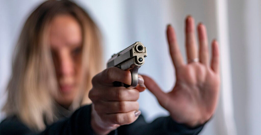 Young blonde woman pointing pistol for self-defense