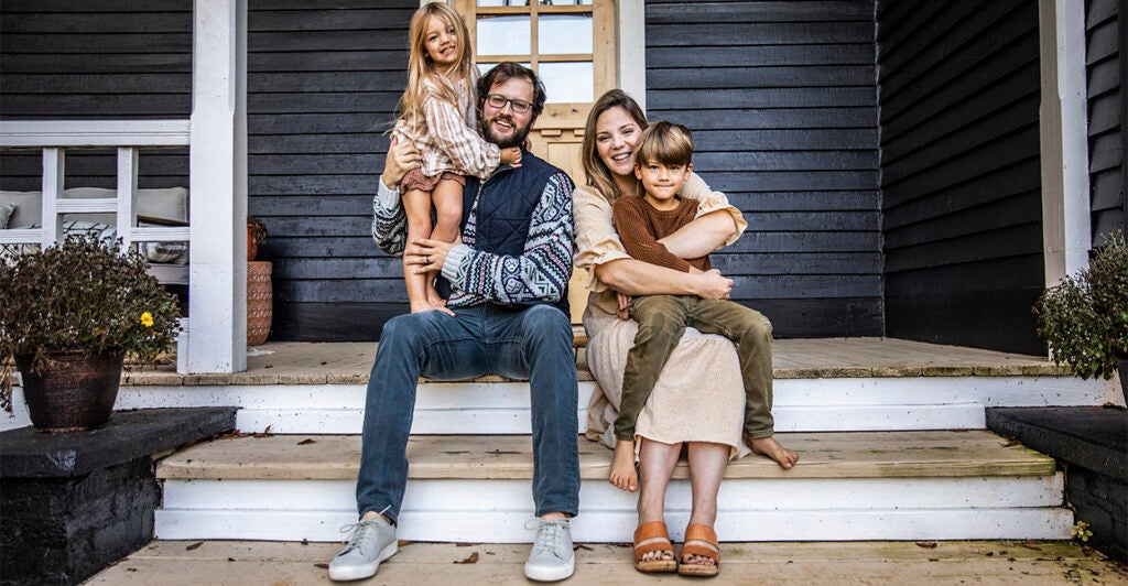 Young family of four sitting on steps in front of house