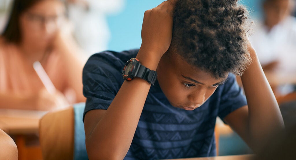 Black male student holds head in hands in classroom.