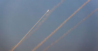 Rockets fly towards Israel against a blue sky.