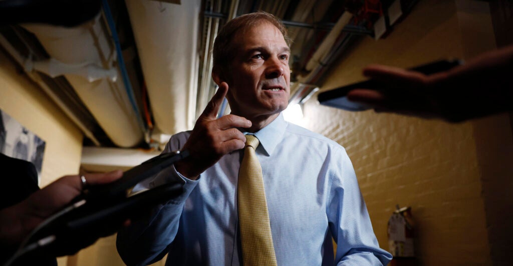 Jim Jordan in a dress shirt with a tie gestures toward the camera.