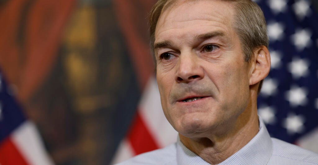 Jim Jordan in a dress shirt stands in front of an American flag