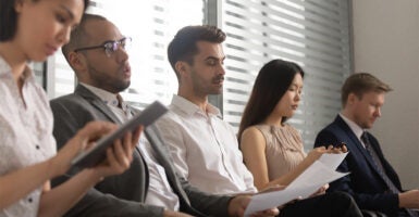 Job applicants of varying races sit in a queue waiting for an interview.