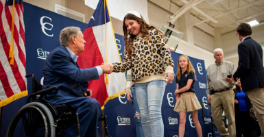 Gov. Greg Abbott in a wheelchair shaking hands with a young student at a rally