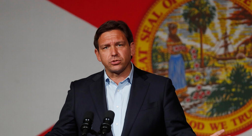 Ron DeSantis in a suit stands in front of the seal of Florida