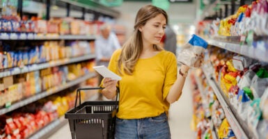 A young woman reads a label in a grocery store aisle.