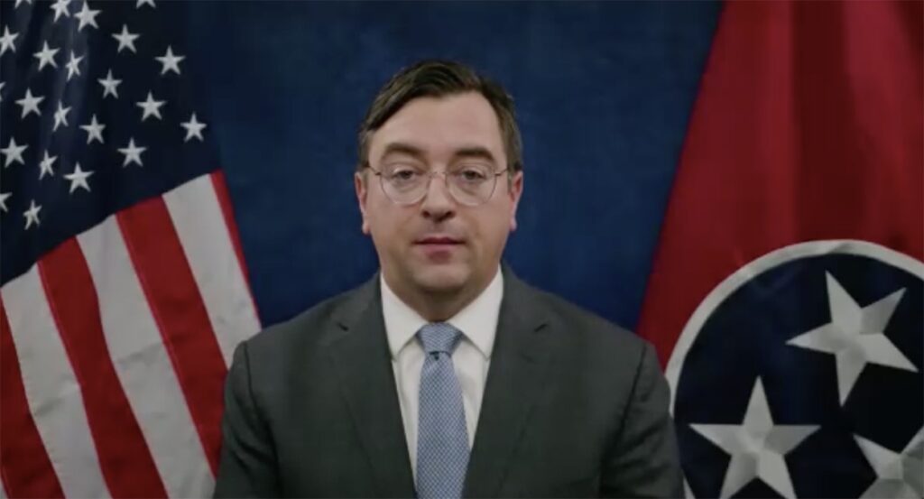 Tennessee Attorney General Jonathan Skrmetti in a suit with an American flag and a Tennessee flag behind him.