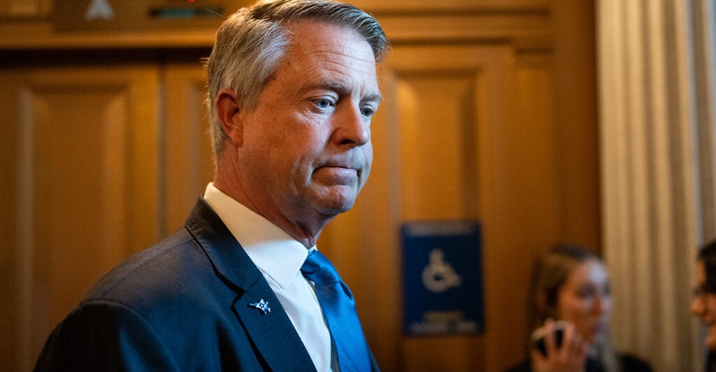 Sen. Roger Marshall, wearing a suit and blue tie, looks down while standing.