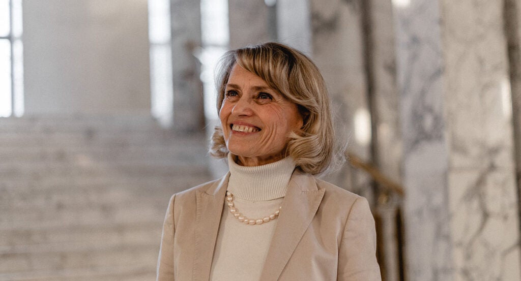 Päivi Räsänen in a tan turtleneck and jacket with a pearl necklace smiles looking up