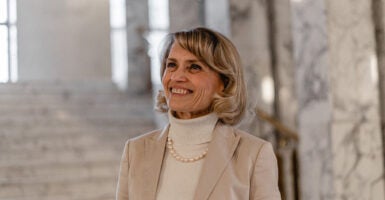 Päivi Räsänen in a tan turtleneck and jacket with a pearl necklace smiles looking up