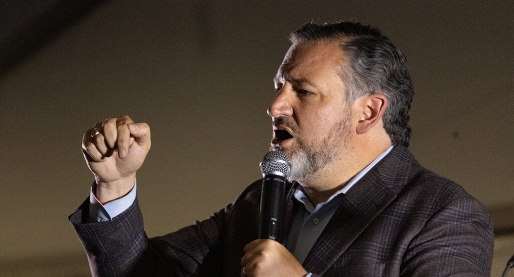 Ted Cruz gestures in a suit holding a microphone.