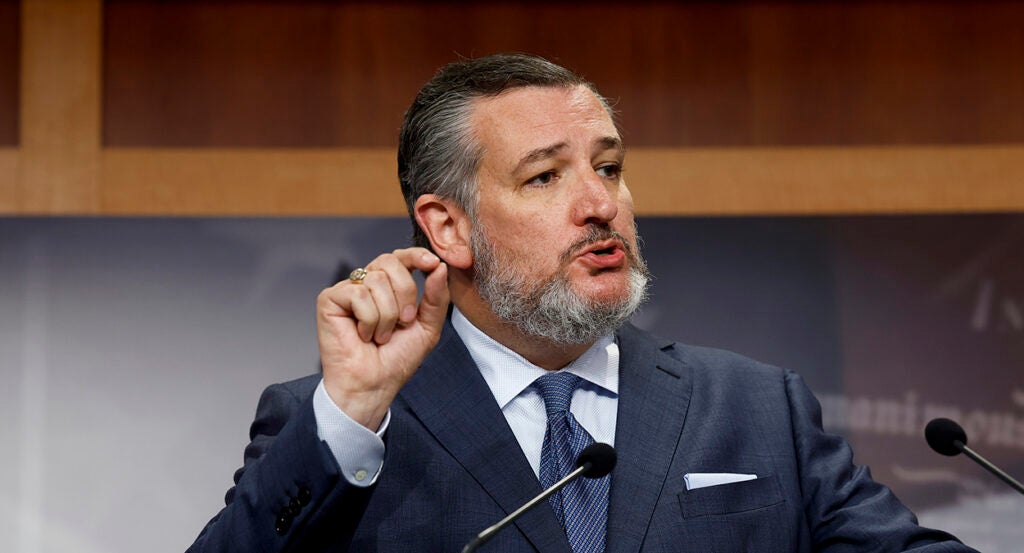 Ted Cruz gestures in a gray suit with a blue tie and wearing a salt-and-pepper beard