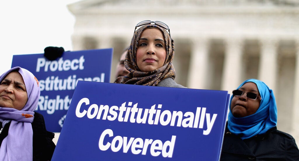 Zainab Chaudry in a headscarf holds a sign in front of the Supreme Court