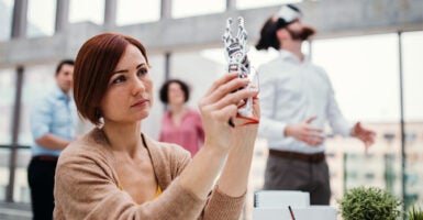 A young female scientist holding up a robotic hand in an office