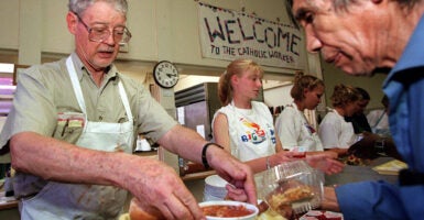 A man and two women serve soup at a soup kitchen