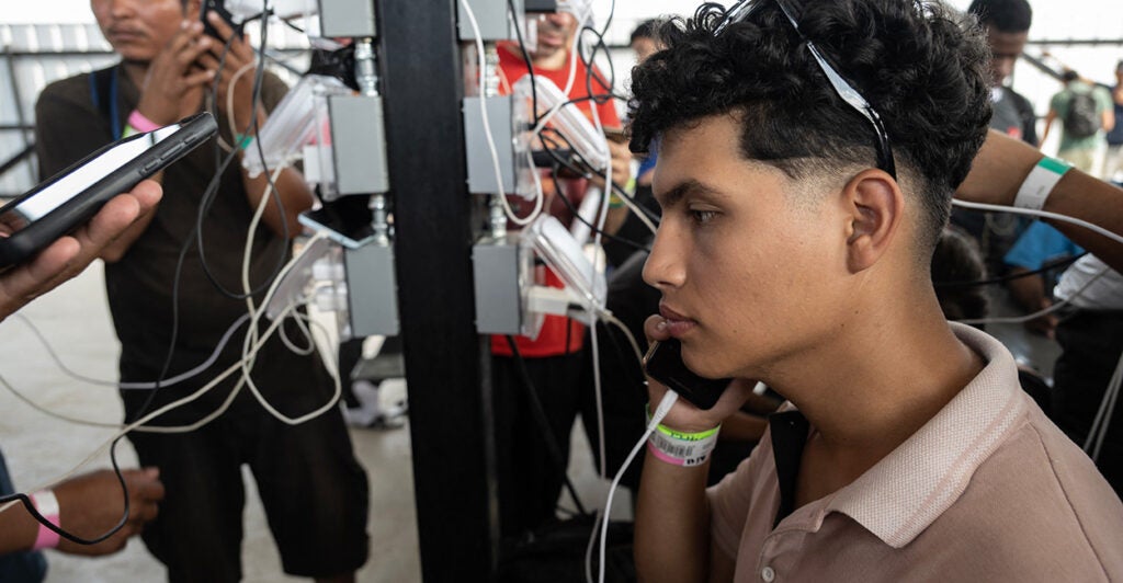 In illegal alien talks on his cell phone by a charging station.