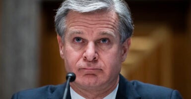 Christopher Wray in a blue suit speaks in front of a microphone