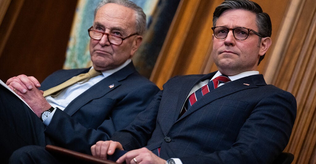 Senate Majority Leader Charles Schumer, D-N.Y., and Speaker of the House Mike Johnson, R-La., sit side by side in suits while attending a Menorah lighting in the U.S. Capitol.