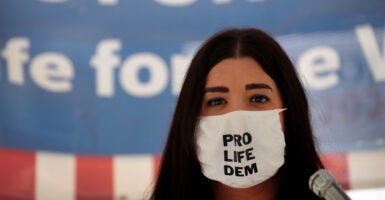 Terrisa Bukovinac stands in front of an American flag while wearing a face mask with the message 