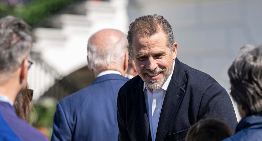 Hunter Biden in a black suit smiles as Joe Biden in a blue suit walks away