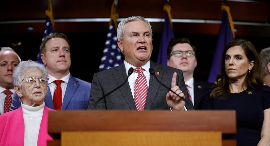 James Comer in a grey suit with a striped tie lifts his left forefinger in the air.