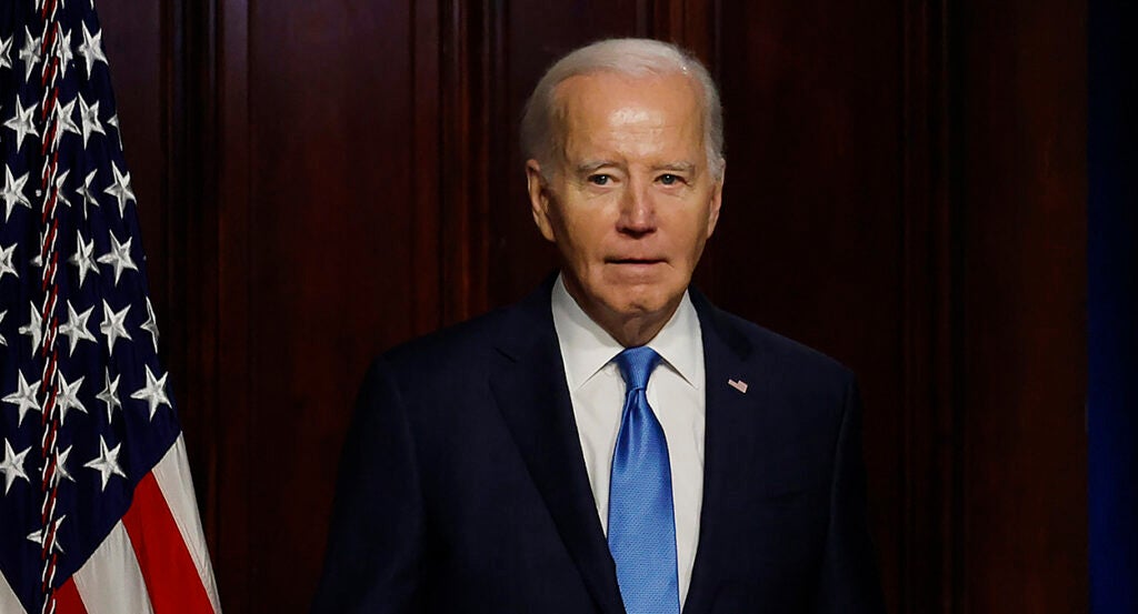 President Joe Biden in a black suit with an American flag pin and a blue tie.