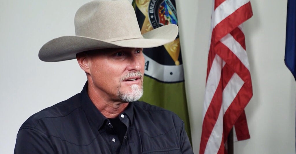 Sheriff Mark Lamb, wearing a cowboy hat, sits talking to The Daily Signal.