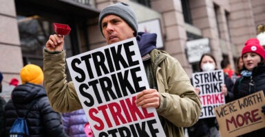 Man in jacket holds sign reading 