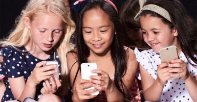 Three little girls sitting together looking at their smartphone screens