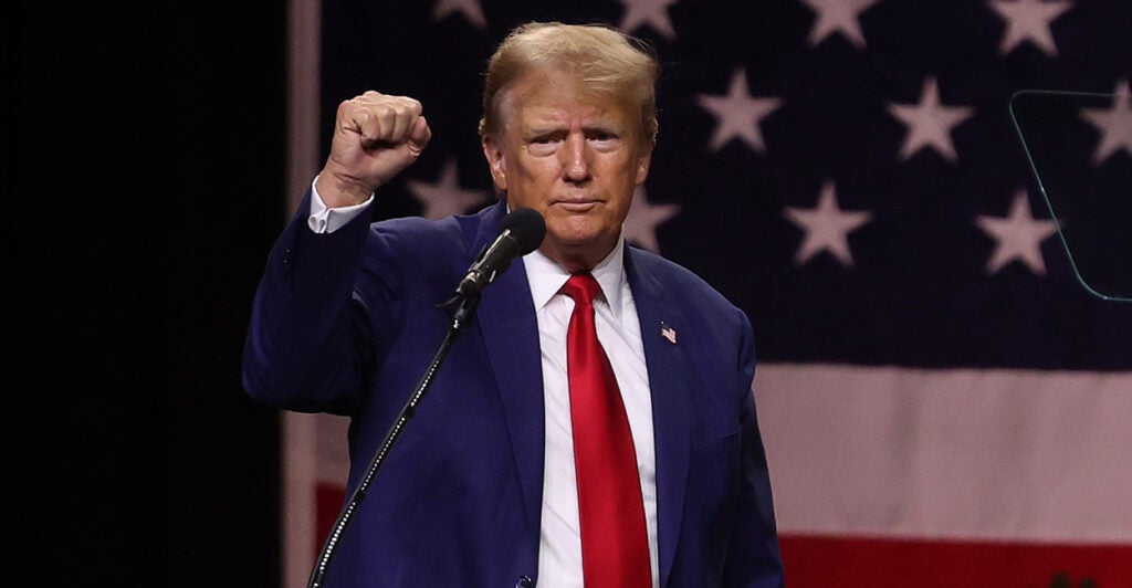 Former President Donald Trump in a suit on stage at campaign rally with fist in the air